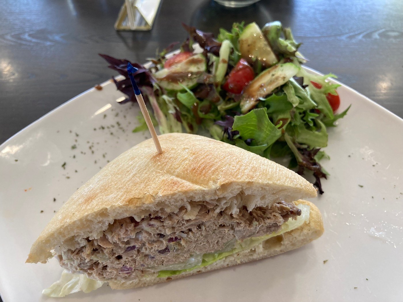 A sandwich with lettuce and shredded filling beside a mixed-leaf, cucumber and tomato salad.